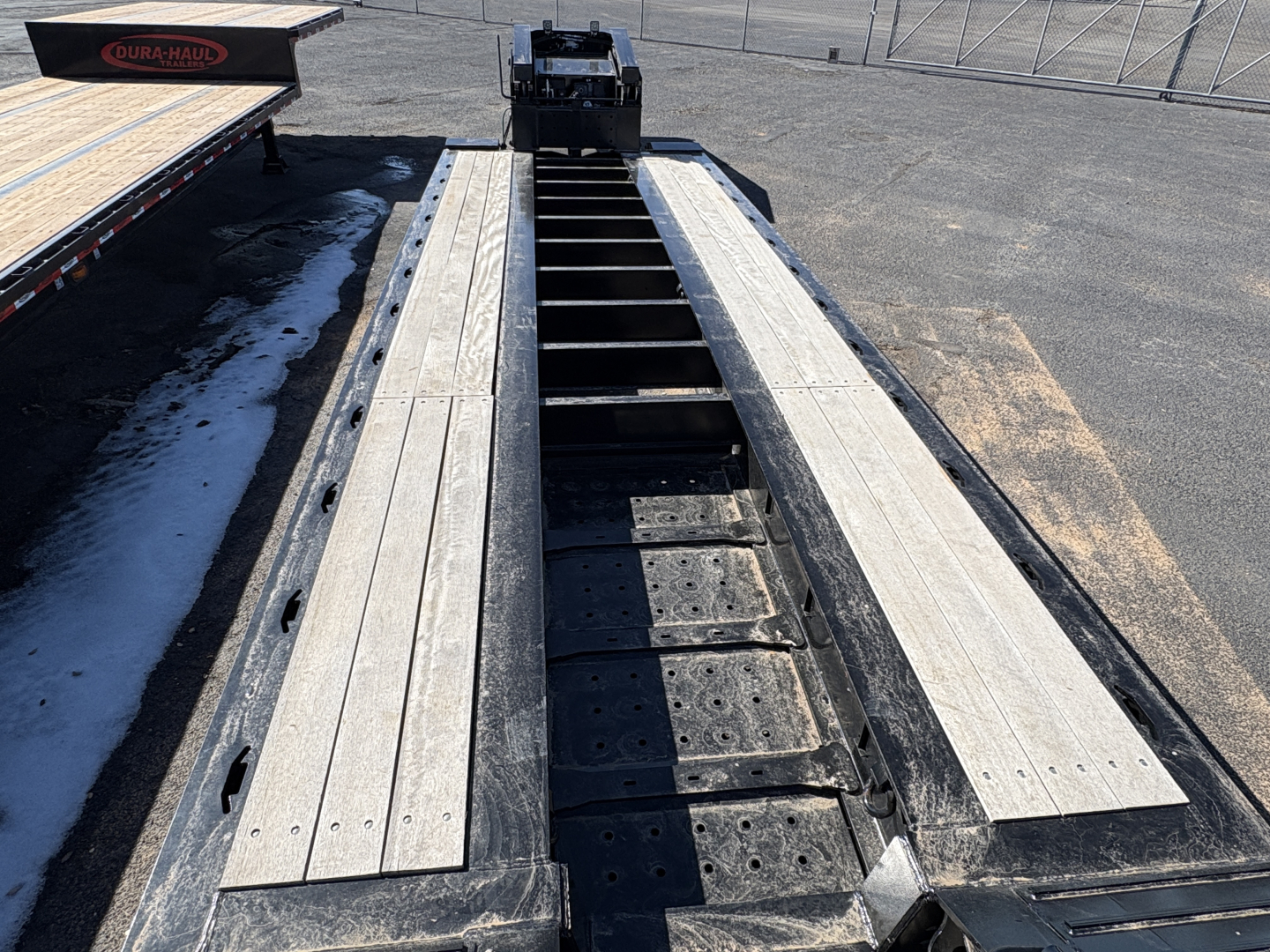 Load King trailer bed with long aluminum floor planks and central gooseneck hitch area visible; steel cross-members and deck screws; wide lowboy layout.