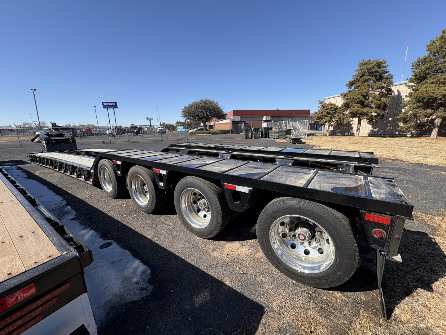 Trailer with multiple axles showing Load King 9-foot wide deck with LDH features; three axles visible with dual wheels, metal frame, and orange warning markers.
