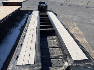 Load King trailer bed with long aluminum floor planks and central gooseneck hitch area visible; steel cross-members and deck screws; wide lowboy layout.