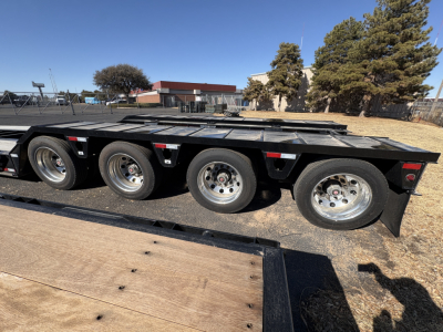 Load King trailer side view showing triple axle configuration and long flatbed deck with black finish and aluminum wheels.