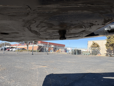 Underbody view of a Load King trailer showing the underside and hitch area with gravel lot and buildings in the background.