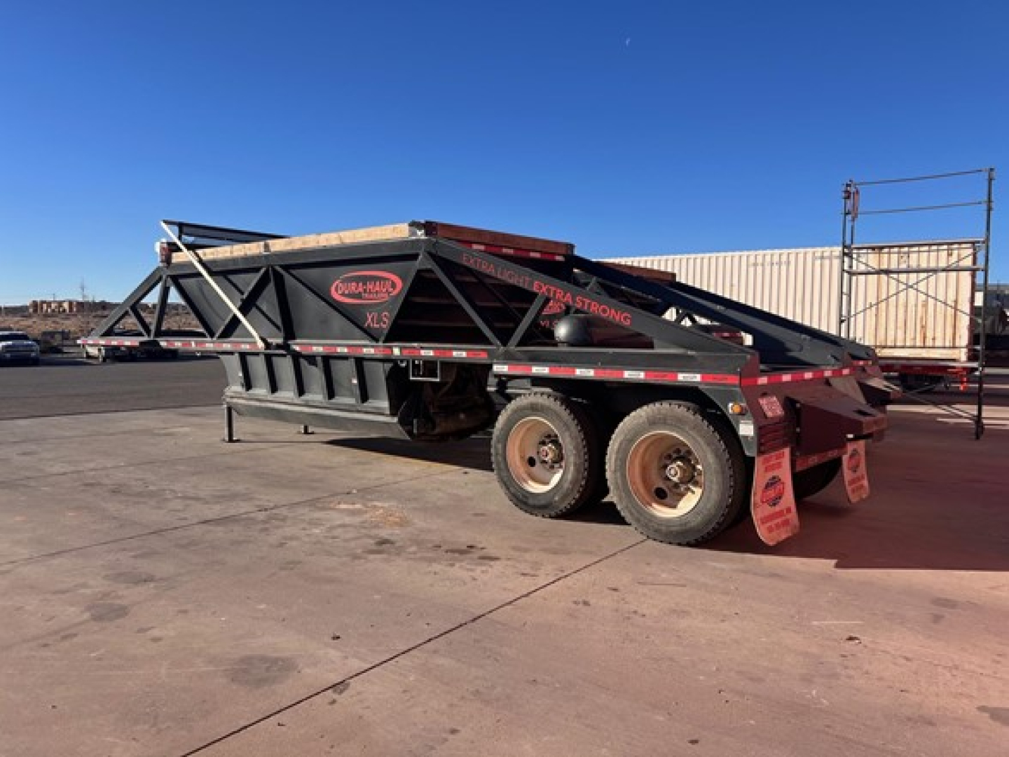 Trailer side view of a 2025 Dura Haul air ride bottom dump with dual rear axles and black structure. Visible markings include Dura Haul logo and reflective tape along the sides.