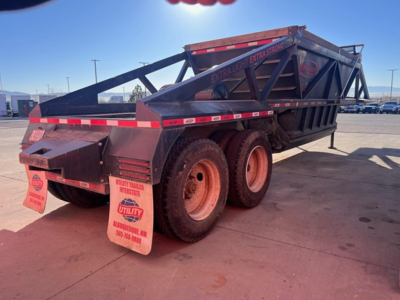 Dump trailer showing dual rear axles and black metal frame with red reflective tape; orange wheels; extra light trailer lettering; hydraulic bottom dump mechanism visible.