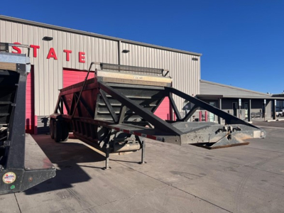 Bottom dump trailer on a lot, black frame with a red top hopper, Stabilizing legs extended, trailer hitch and ramp frame visible in front.