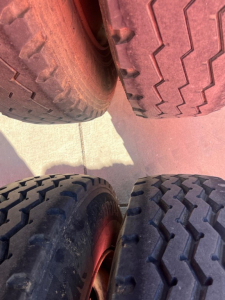 Bottom dump trailer tires close-up showing tread patterns and sidewalls; angled view with red rims and dusty concrete surface.