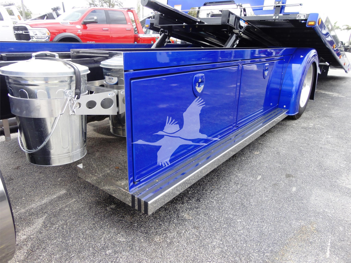 Blue Peterbilt rollback truck side with fuel tank and graphic logo showing white bird silhouette on door panel.