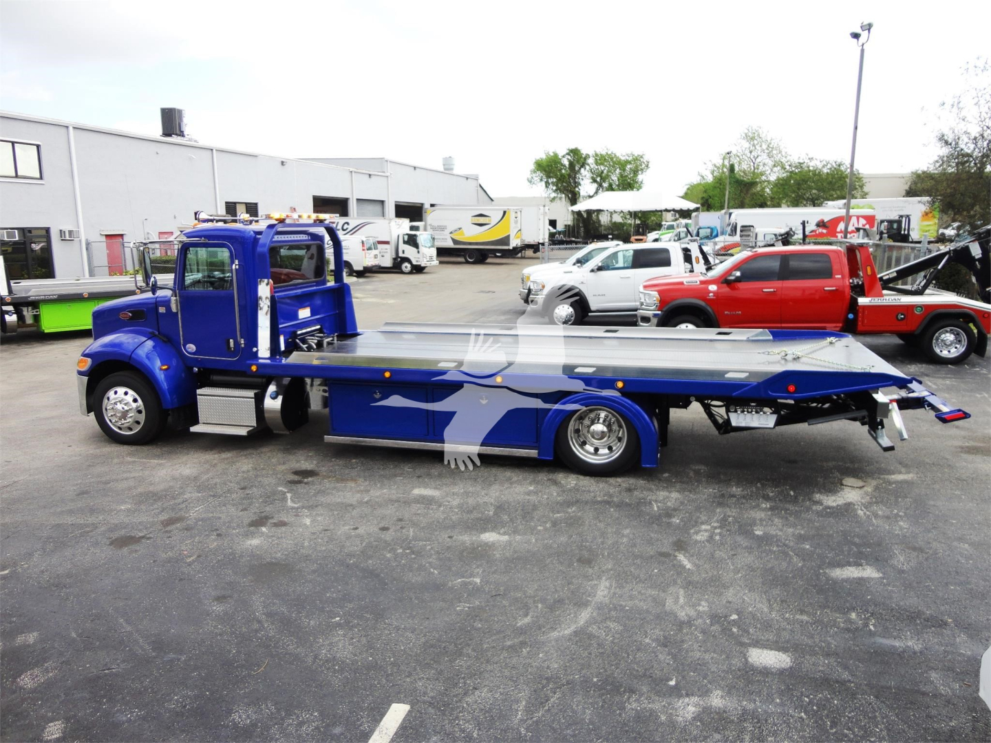 Peterbilt 337 rollback tow truck in blue showing long flatbed and cab side view.