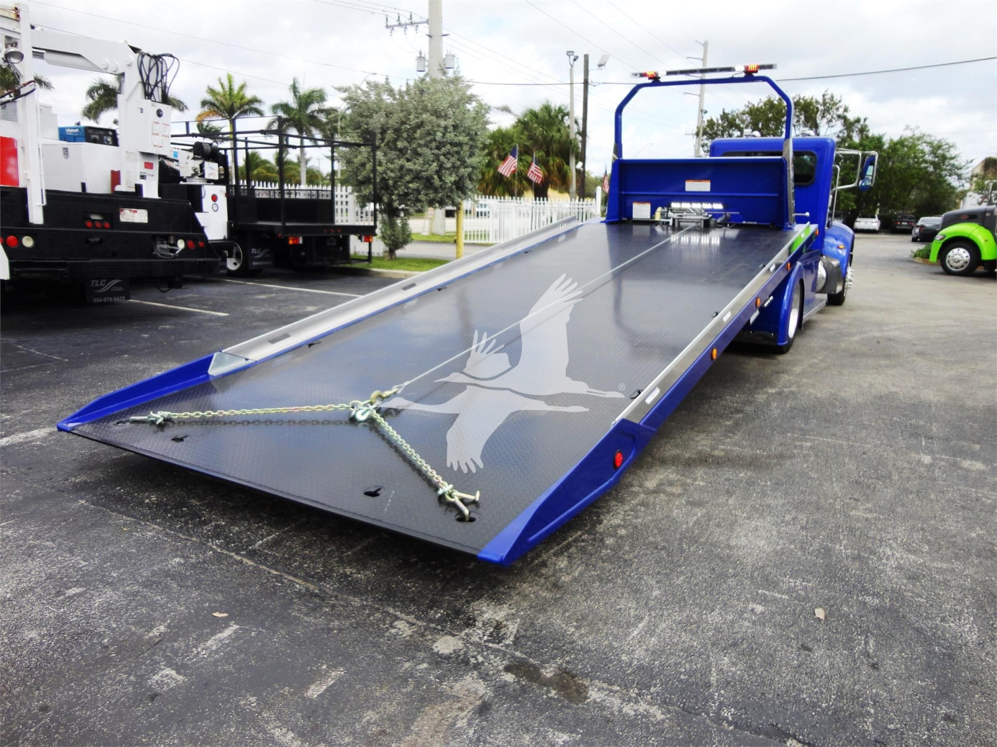 Truck deck of a blue 2022 Peterbilt 337 rollback showing a lowered flatbed with chain tie-downs and a decorative graphic on the surface.