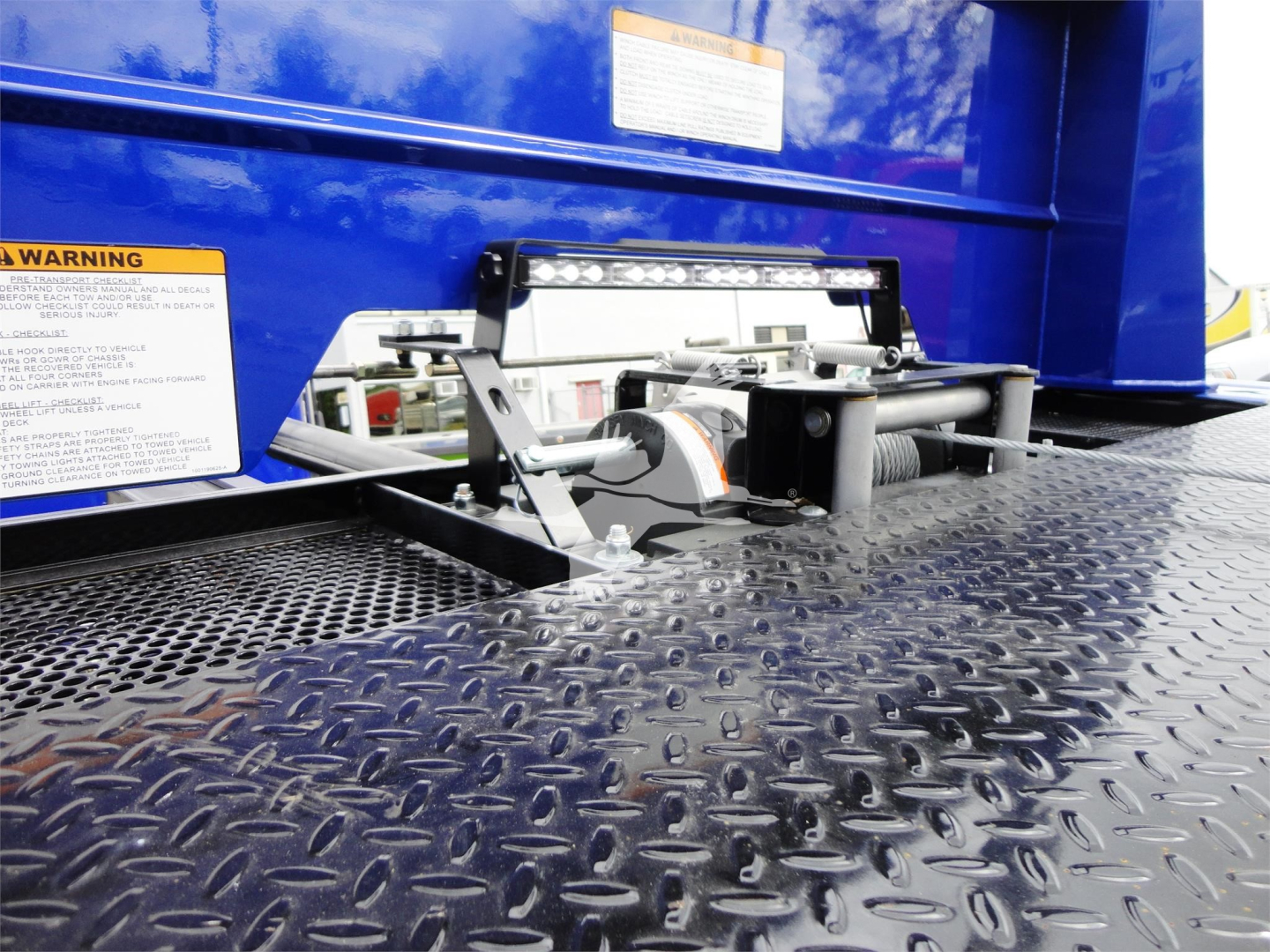 Peterbilt 337 rollback truck platform with metal diamond plate deck and a mounted light bar; warning labels visible on blue body panels.