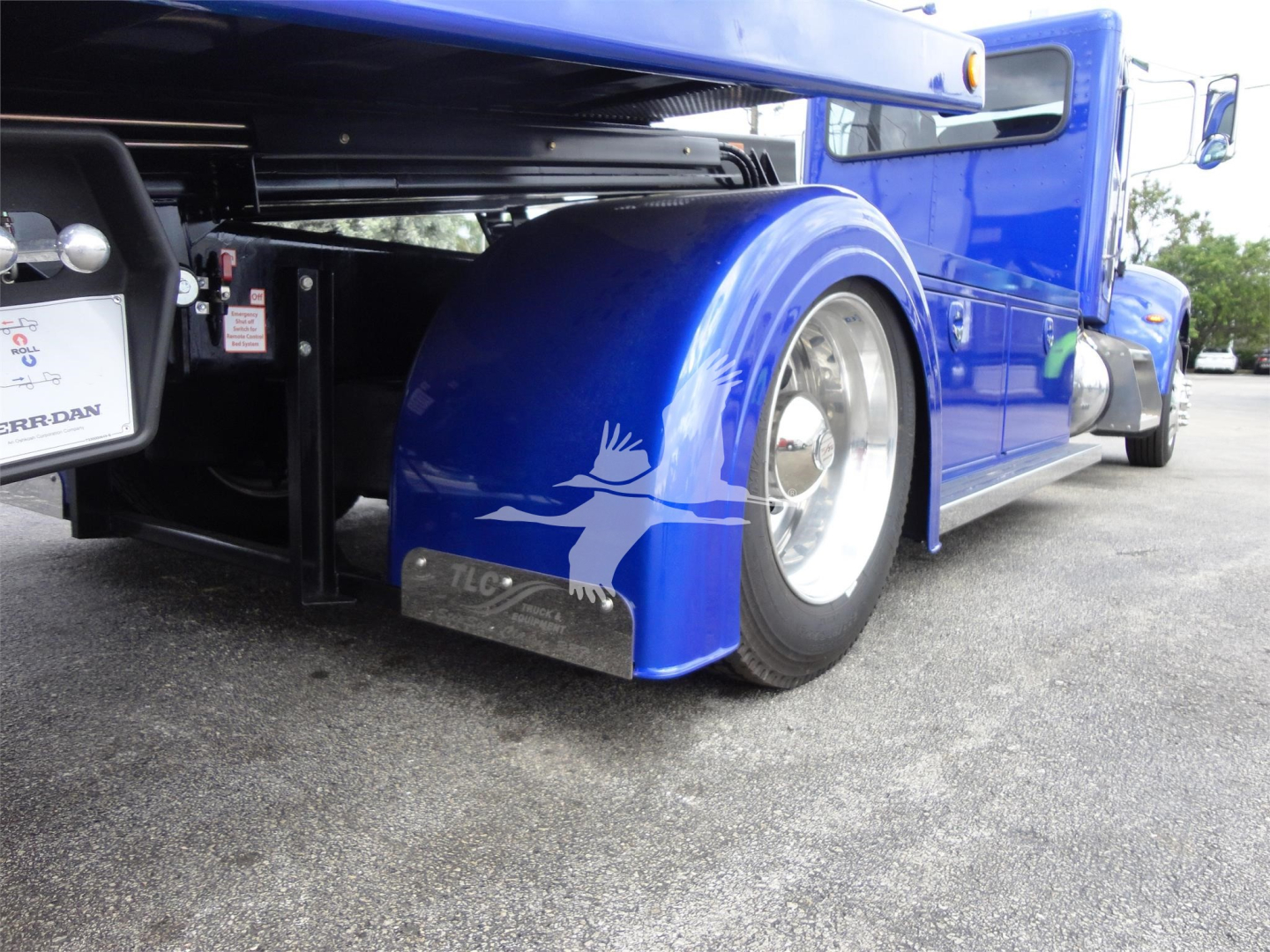Rear side of blue Peterbilt 337 rollback truck showing fender, wheel, and side panel. Visible text on plate near rear shows 'FERRA' and additional small labels; wheel well and mudguard are prominent.