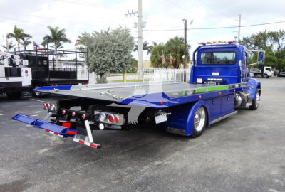 Tow truck with blue rollback bed and extended rear ramps; rear lights and hydraulic equipment visible.