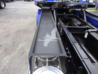 Truck bed area of a 2022 Peterbilt 337 rollback showing a metal slide-out or equipment tray with a textured surface and a circular hydraulic component visible beneath.