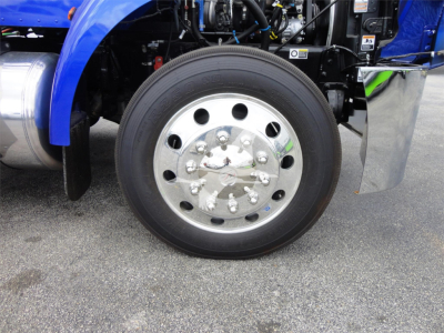 Truck wheel and front fender area showing chrome hubcap with multiple lug nuts on a Peterbilt 337 front axle.
