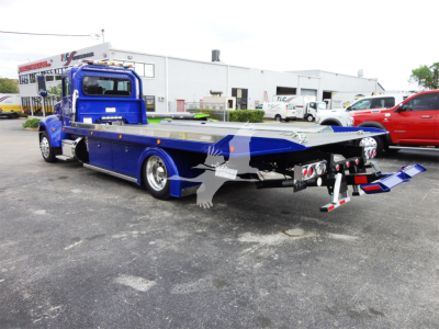 Blue Peterbilt 337 rollback truck shown from side-rear angle with flatbed and towing equipment extended.