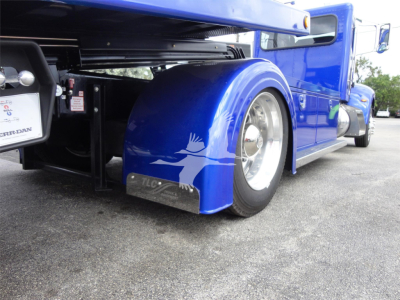 Rear side of blue Peterbilt 337 rollback truck showing fender, wheel, and side panel. Visible text on plate near rear shows 'FERRA' and additional small labels; wheel well and mudguard are prominent.