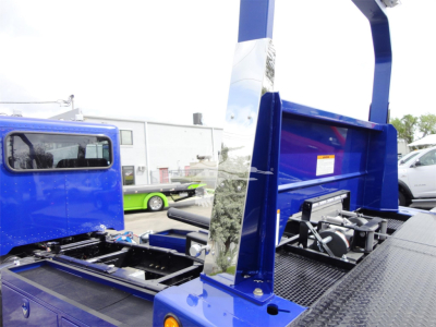 Blue Peterbilt 337 rollback truck chassis with hydraulic platform and control levers visible.