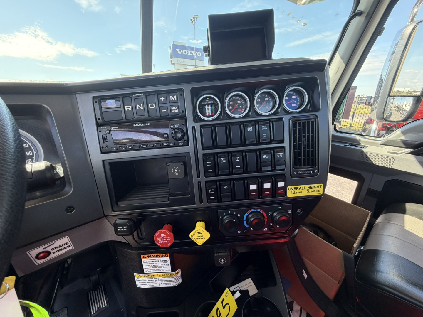 Dashboard of a 2026 Mack GR64F crane truck showing instrument cluster, control switches, and warning labels.