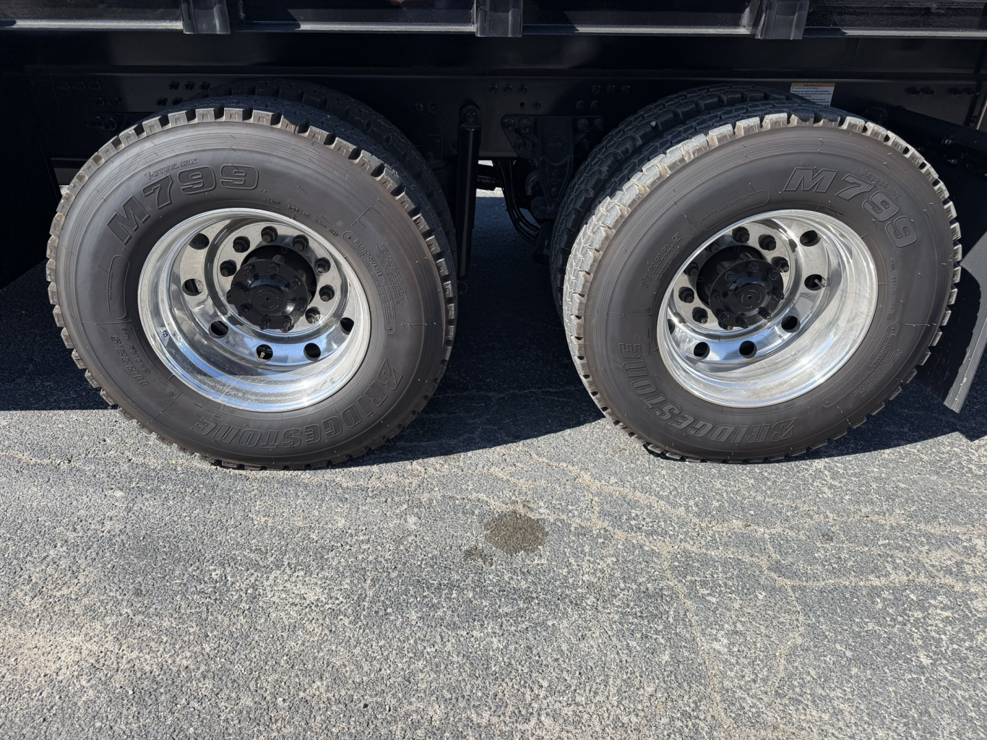 Dual rear axles with M60 tires and chrome wheels under a Mack GR64F crane truck showing tire treads and wheel hubs.