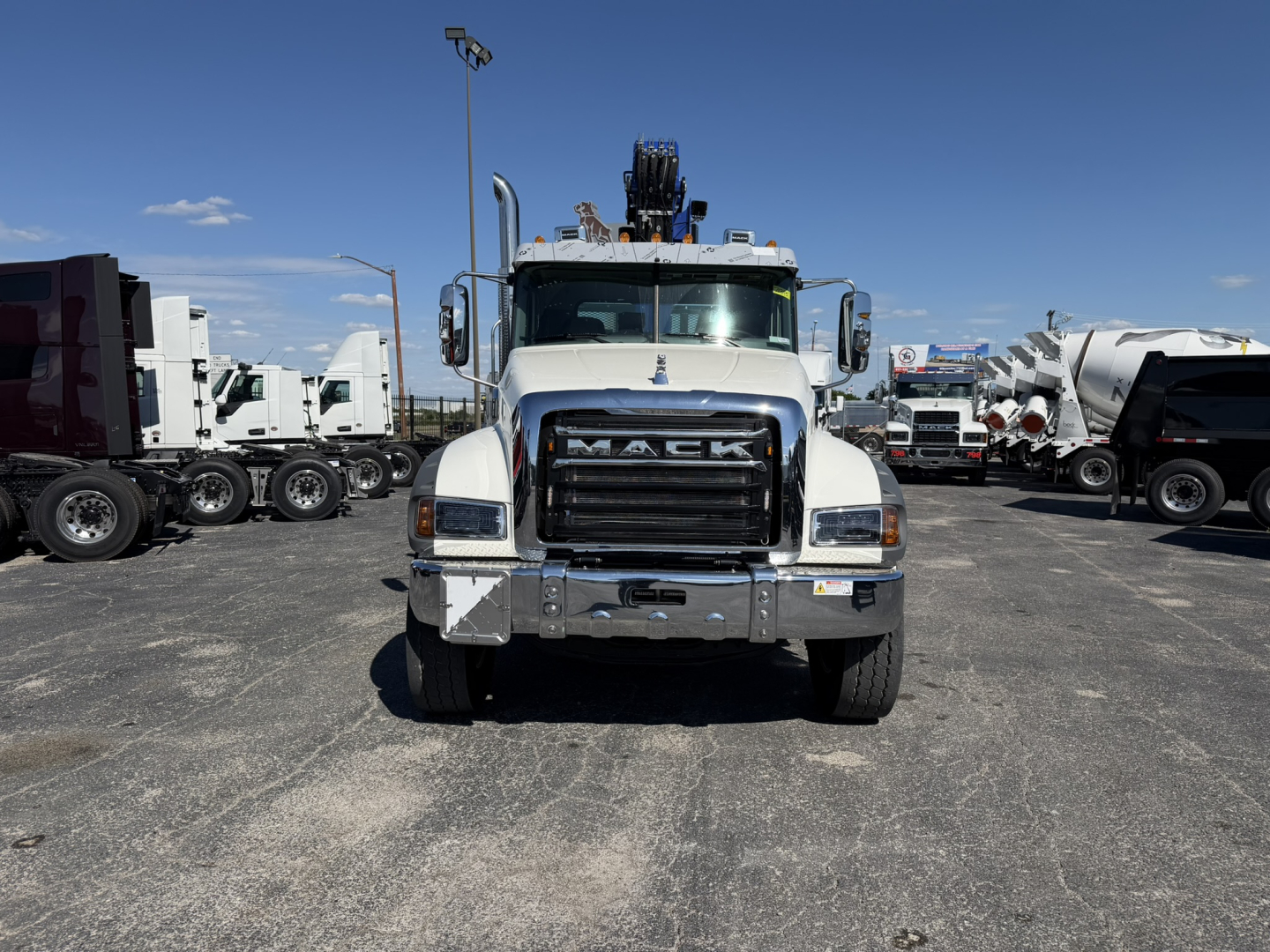 Front view of a white Mack GR64F heavy-duty truck with a prominent grille, bumper, and crane equipment on top.