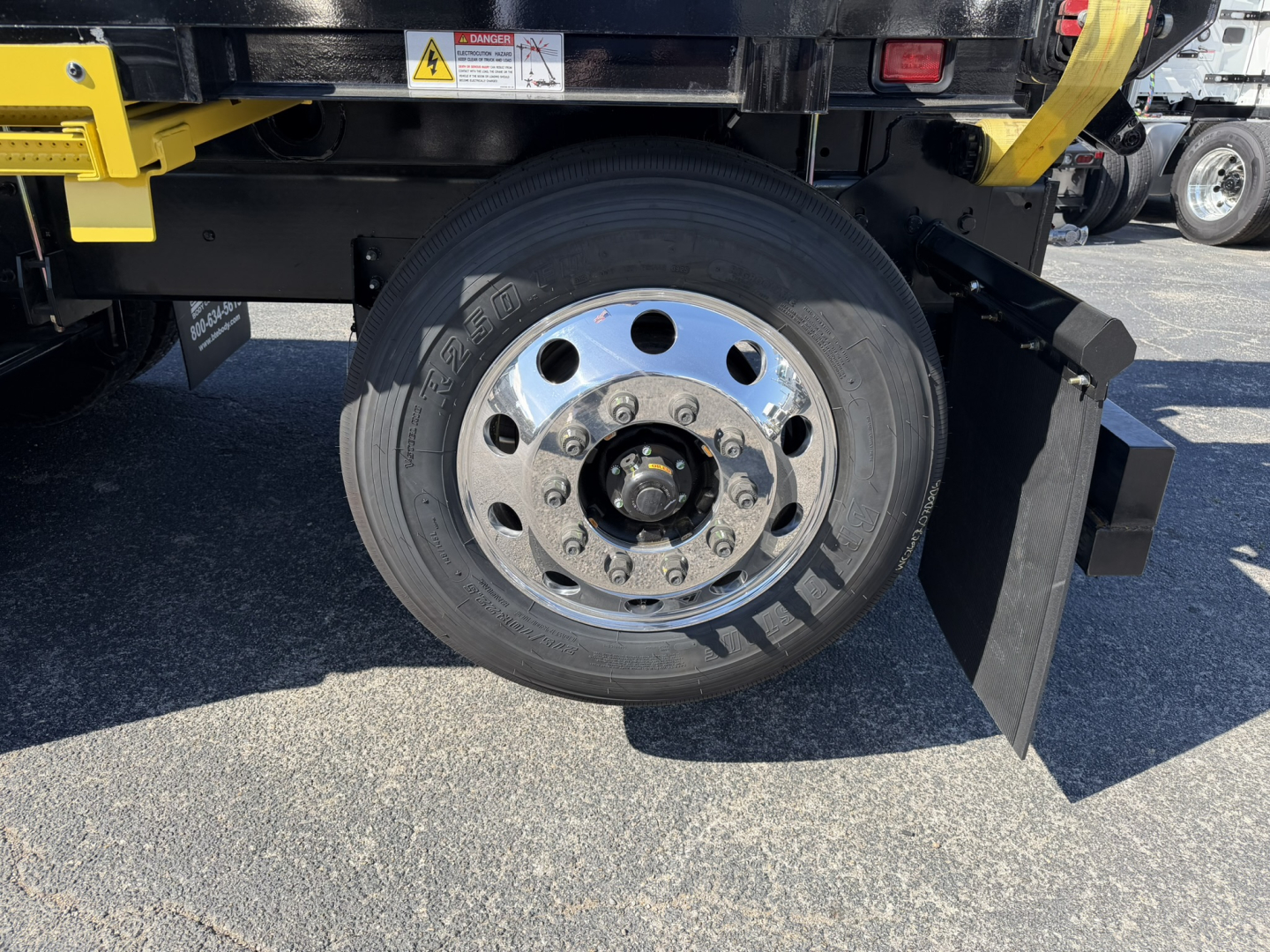 Mack GR64F truck wheel and hub assembly with chrome lug nut cover, black tire, and partial undercarriage.