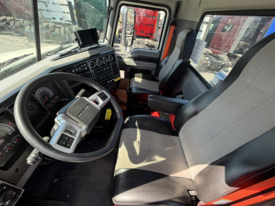 Interior of a 2026 Mack GR64F crane truck cab showing steering wheel, gauges, and two front seats with light gray and black upholstery, large side window, and control monitor on dash.