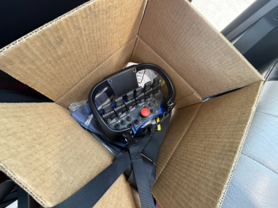 Crane control pendant in a cardboard box, visible levers and red emergency stop button.