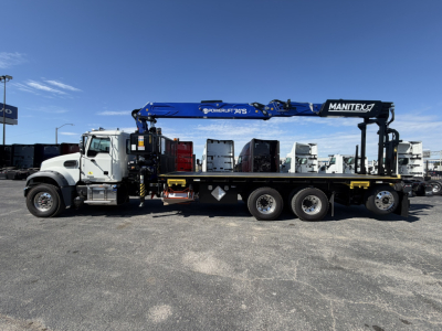 Truck-mounted crane on a Mack GR64F flatbed tow truck with a blue Manitex boom extended, side view showing cab and dual rear axles.