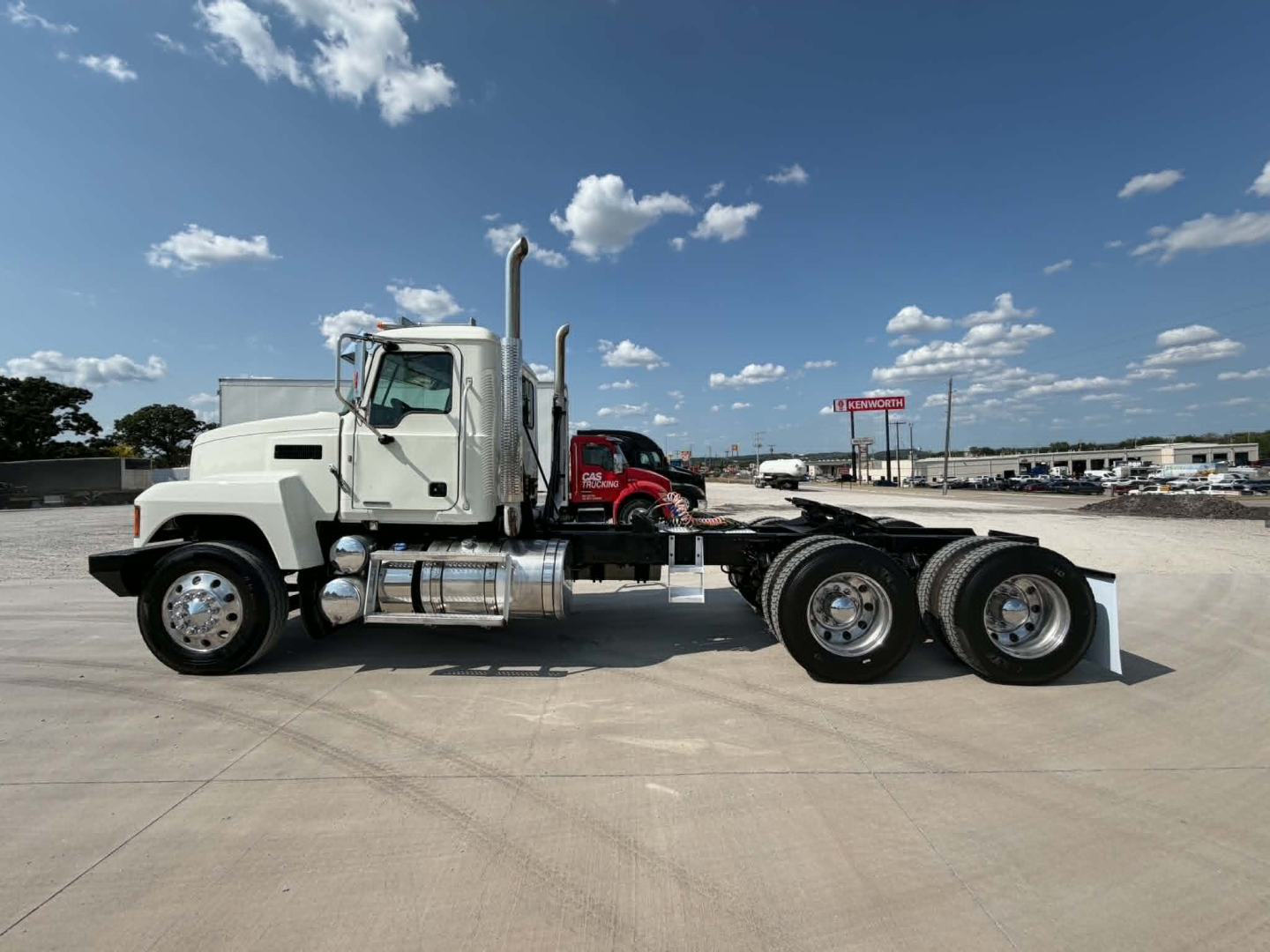Truck side view showing dual rear axles and chrome fuel tanks; cab with white paint and vertical exhaust; no visible detailed text on components.