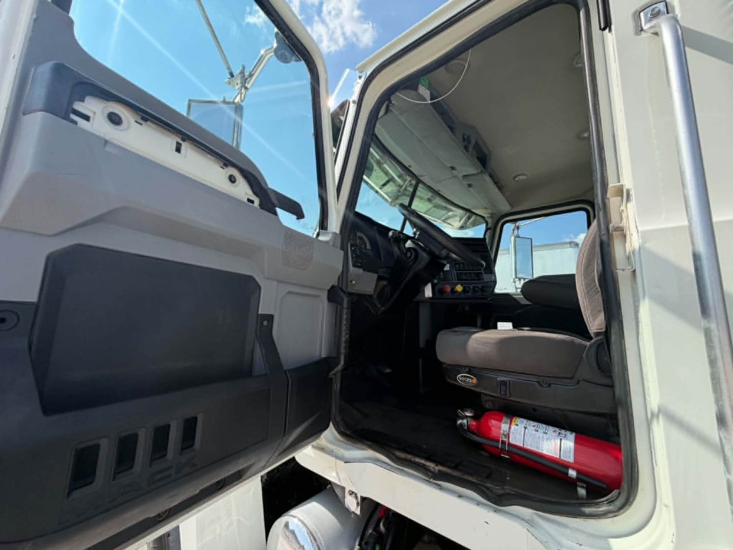 Cab interior of a 2019 Mack CHU613 truck with open driver door showing steering wheel, dashboard, and a fire extinguisher under the seat.