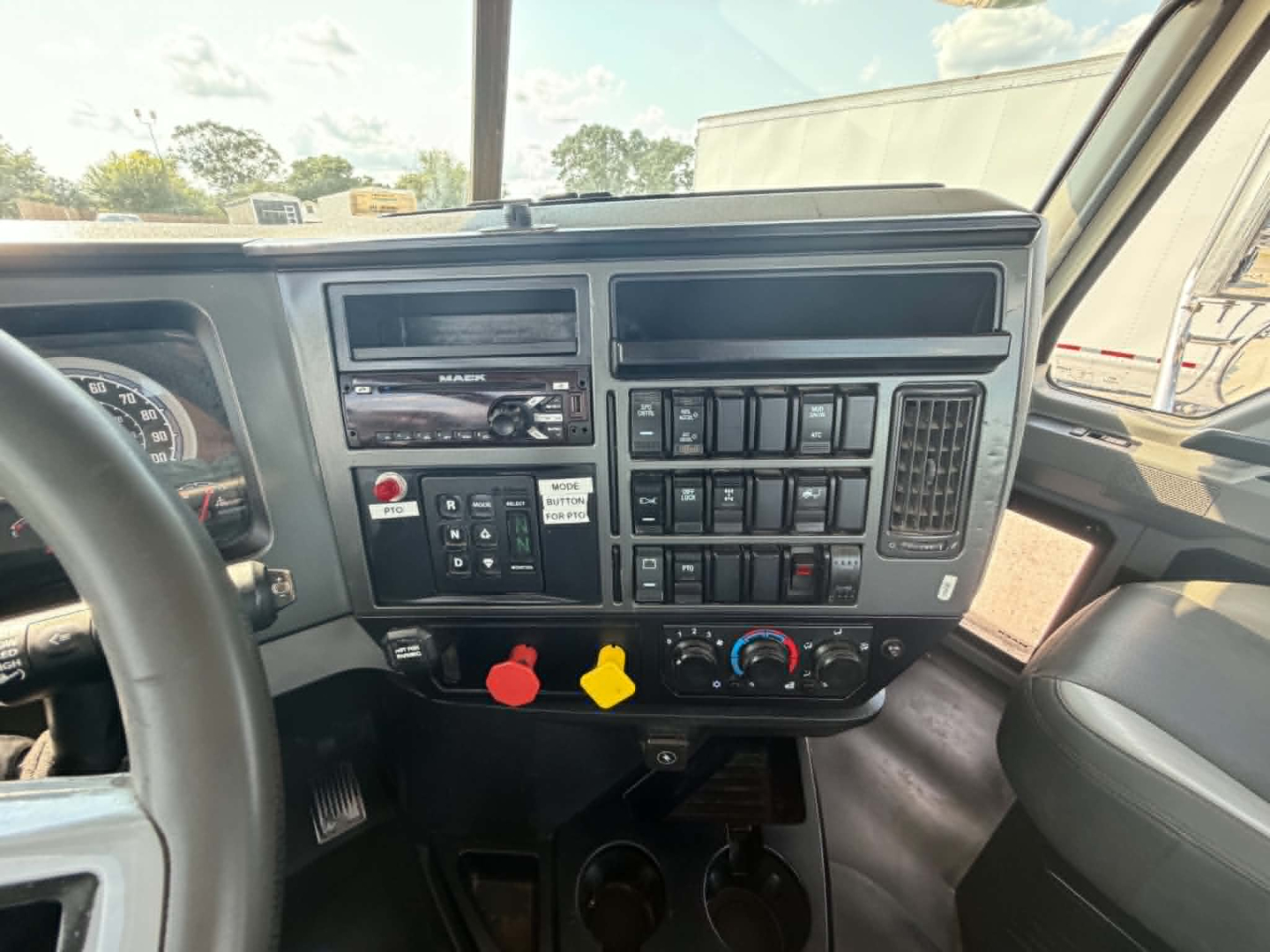 Mack CHU613 cab interior showing instrument cluster, control panel, switches, and dual cup holders. Dashboard features include radio, climate controls, and red/yellow knobs.