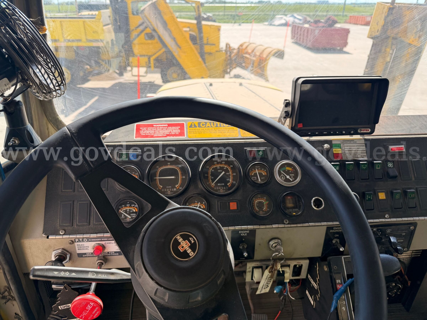 Oshkosh PA-2323-SP cab interior showing steering wheel, gauge cluster, and monitor; dashboard with switches and warning labels visible.