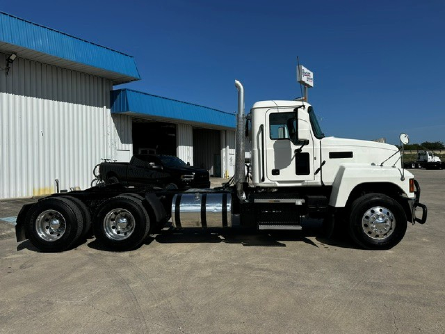 Truck showing white 2020 Mack PI64T conventional daycab, side view with sleeper cab, dual rear axles, chrome fuel tanks, and black chassis.