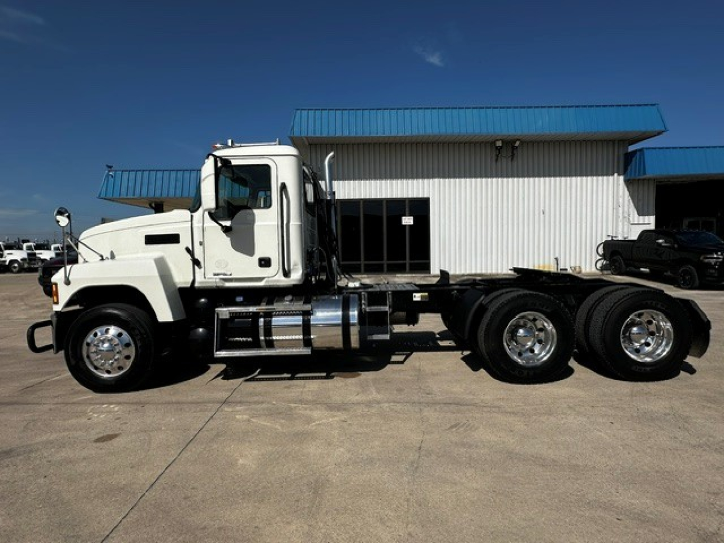 Truck side view of a 2020 Mack PI64T conventional daycab showing white cab, chrome fuel tanks, dual rear axles, and large wheels.