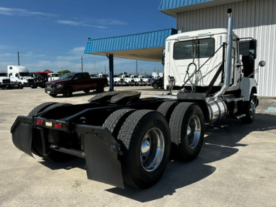 Truck chassis with tandem rear axles and sleeper-less cab, white Mack PI64T, dual exhaust stacks, various hoses and fuel tanks visible.
