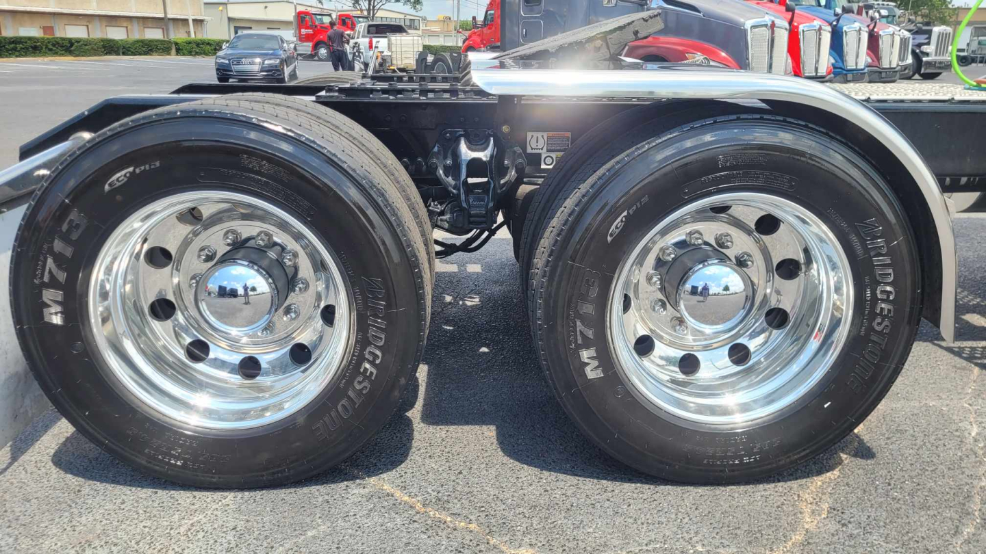 Kenworth W900L rear dual-axle wheels and chrome rims showing Mud tires and hubcaps in a truck yard.