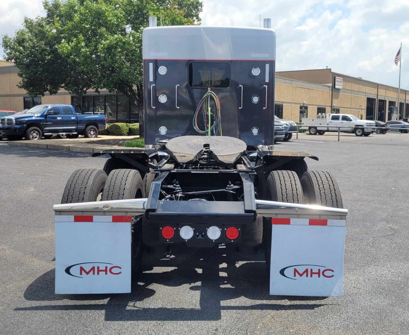 Kenworth W900L truck rear view showing dual rear axles, chassis, and mud flaps with MHC logo.