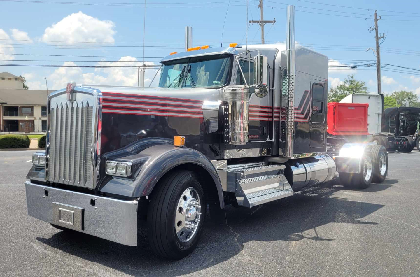 Kenworth W900L conventional sleeper truck in dark color with red and maroon stripes, chrome bumper and steps, large grille, dual rear axles.