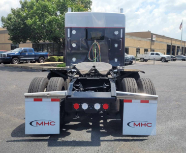 Kenworth W900L truck rear view showing dual rear axles, chassis, and mud flaps with MHC logo.