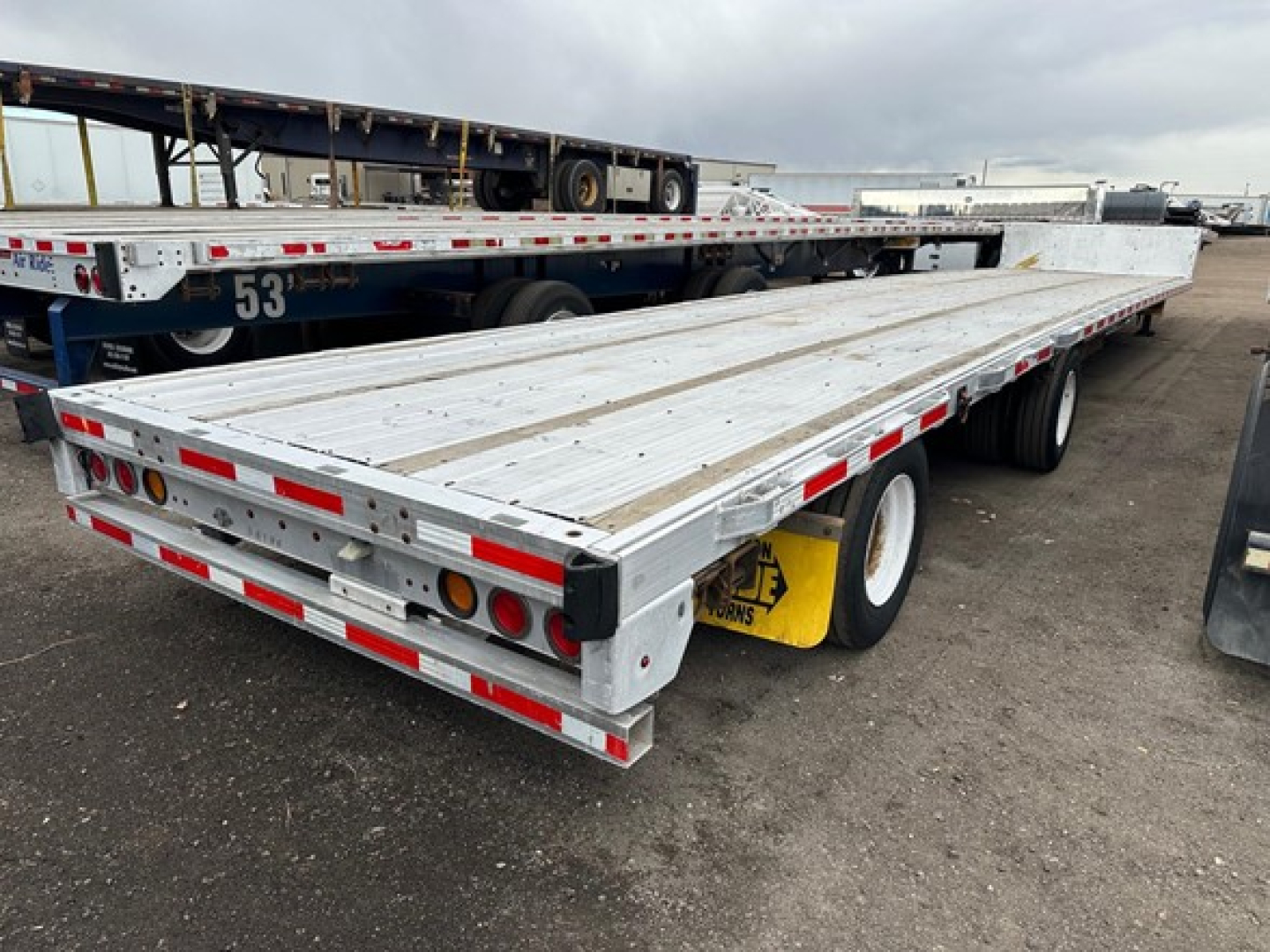 Trailer bed of a 2015 Trail King Tk Drop Deck flatbed trailer showing long aluminum deck, rear lights, reflectors, and dual rear wheels.