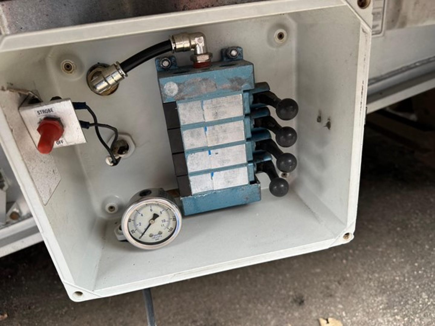 Drop deck trailer control manifold with blue valve block, pressure gauge, and red stop/start switch labeled 'STOP' in a white panel.