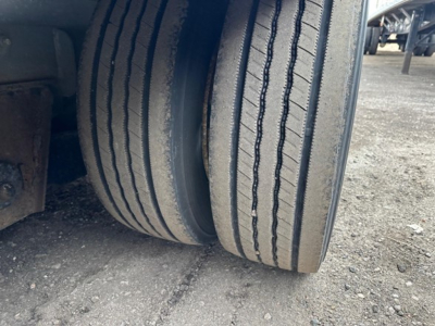 Trailer wheel view showing dual tires with tread and sidewall details on a drop deck trailer.