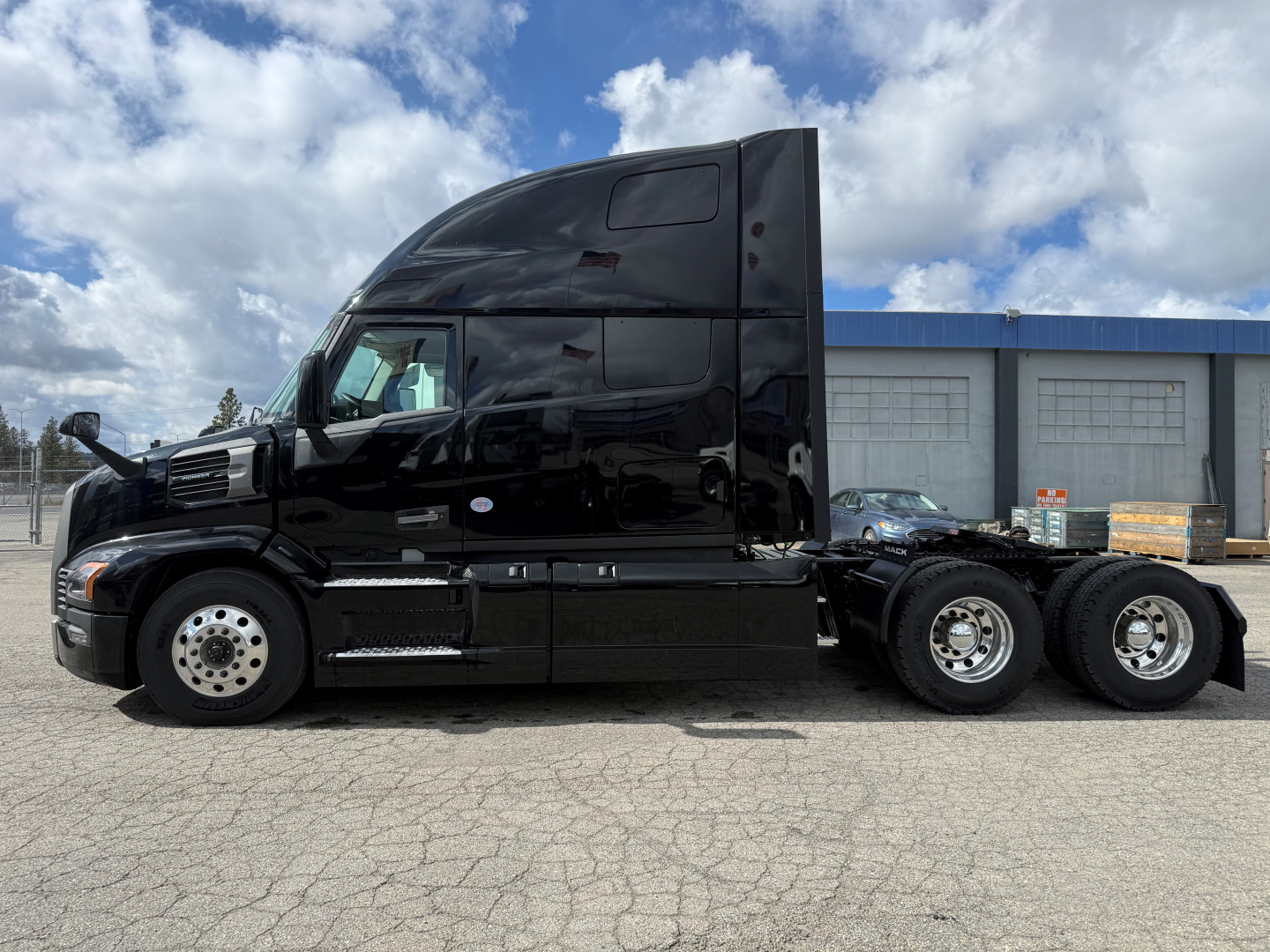 Truck side view showing a black 6x4 semi tractor with sleeper cab, chrome wheels, three rear axles, no visible text.