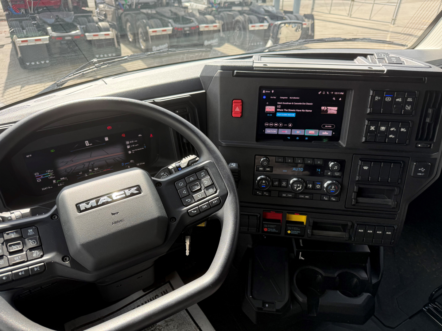Mack PR64T76H truck cab interior showing steering wheel and dashboard with touchscreen display and controls.