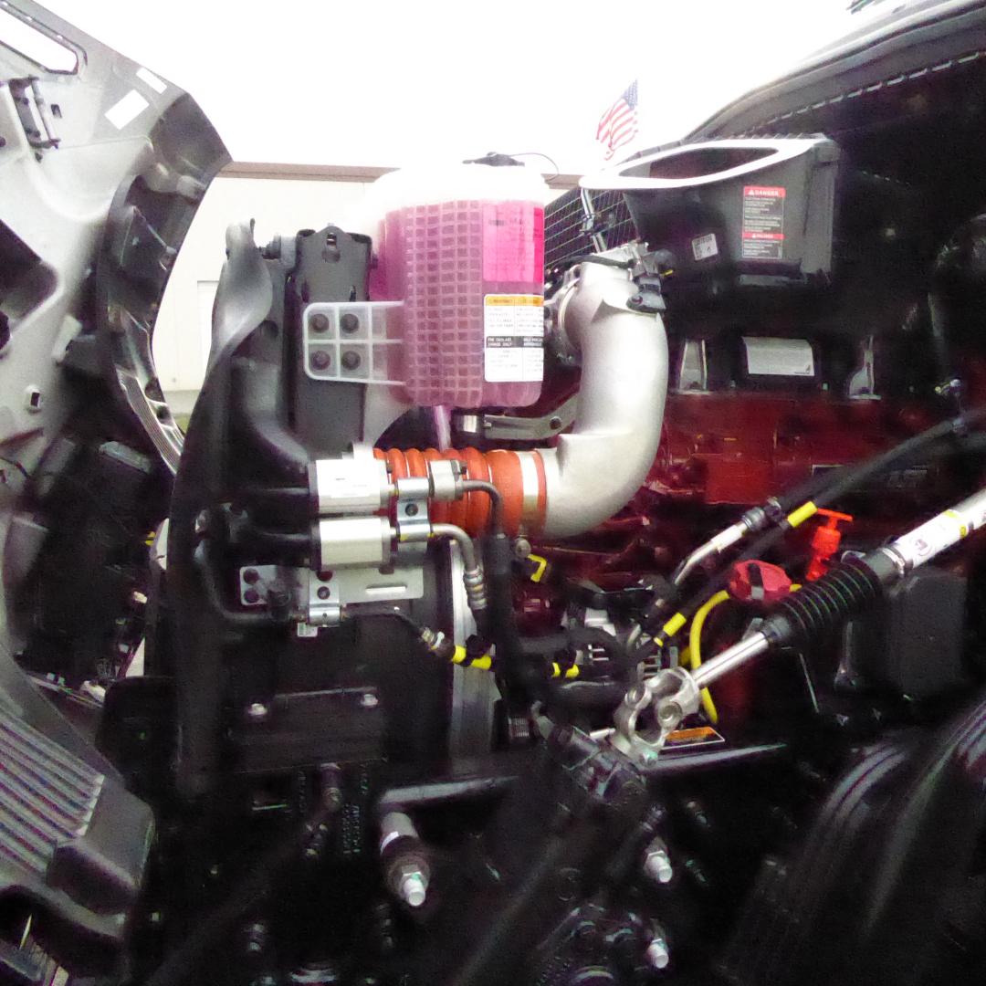 Engine bay of a new Mack PR64T76H truck showing pink air intake filter, turbo piping, hoses, and surrounding components.