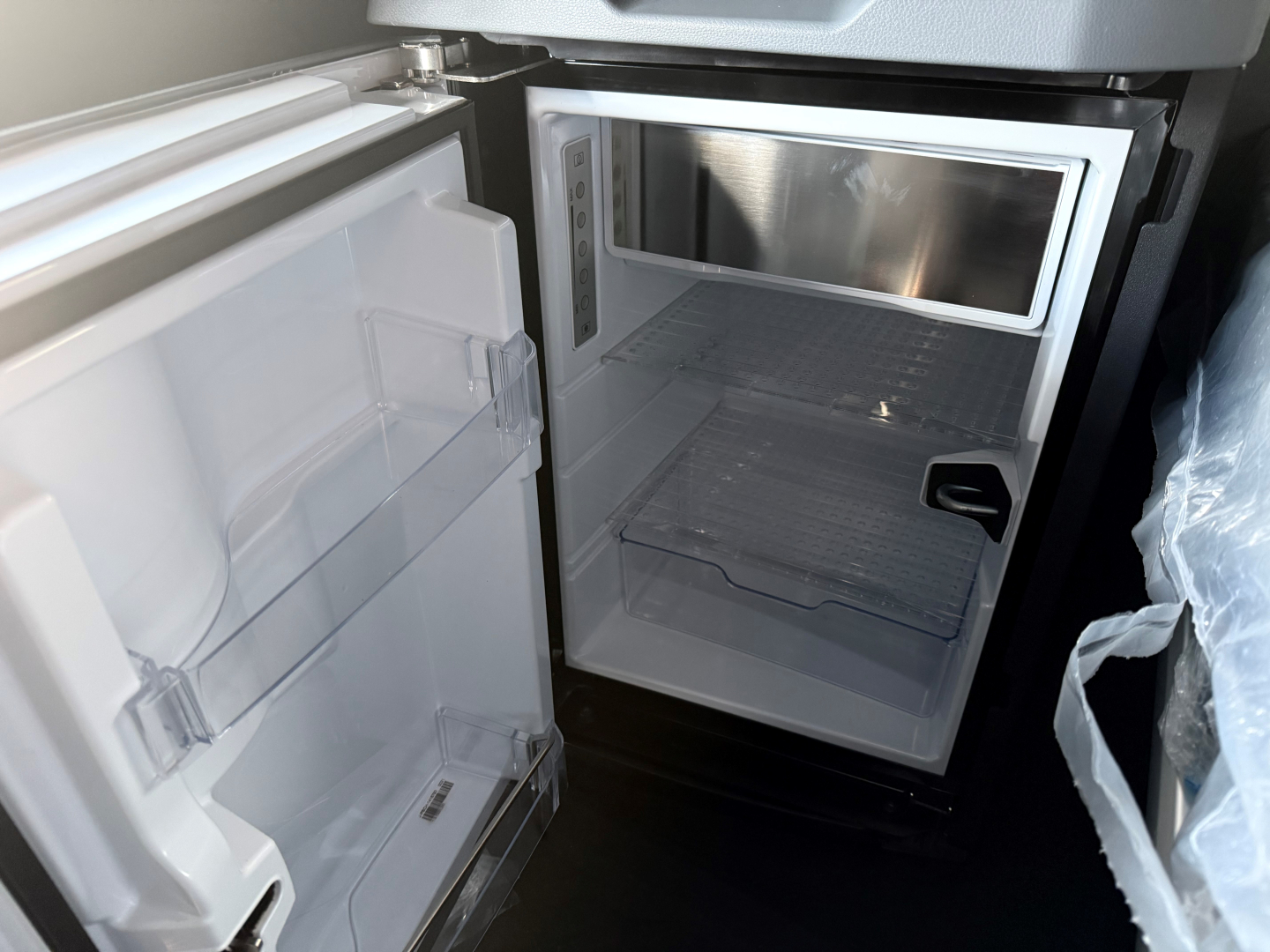 Fridge inside a Mack PR64T76H sleeper cab showing open small refrigerator unit with empty shelves and microwave above it.