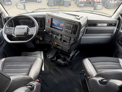 Mack PR64T76H truck cockpit showing steering wheel with Mack logo, dashboard with touchscreen display, controls, and two front seats.