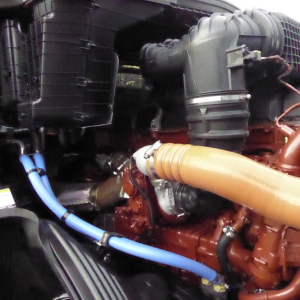 Truck engine bay showing orange turbocharger hose and blue high-pressure hose attached to a red diesel engine.