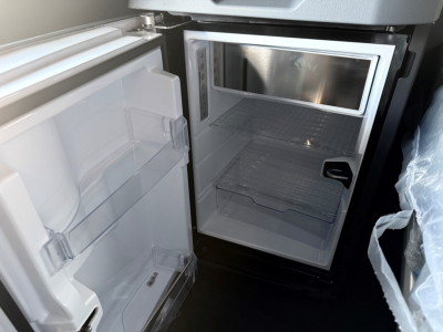 Fridge inside a Mack PR64T76H sleeper cab showing open small refrigerator unit with empty shelves and microwave above it.