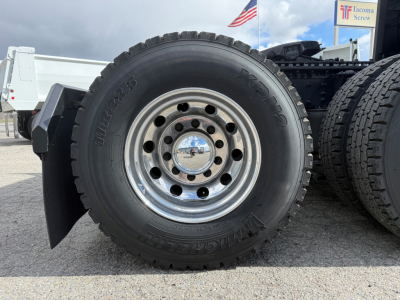 Mack PR64T76H truck wheel close-up: large black tire with chrome hub, dots of lug nuts, and tread visible.