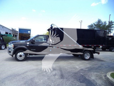 Ram 5500 dump truck in service position showing front cab and long black dump bed with white lettering and chrome wheels.